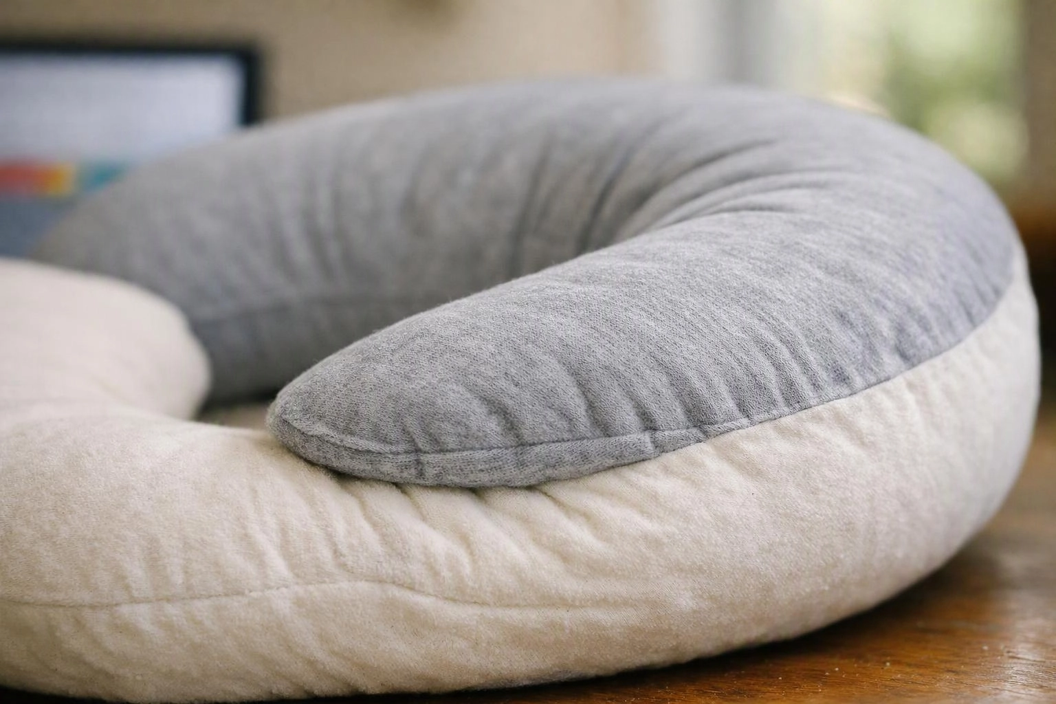 A gray and white U-shaped cushion sits on a wooden table in a softly lit room
