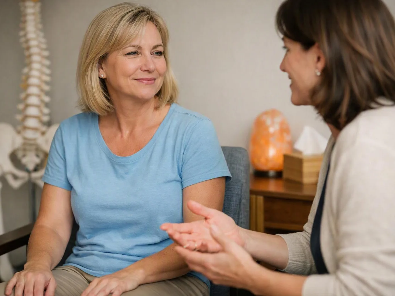 Two women sit talking in a calm room, one smiling while the other gestures with her hands